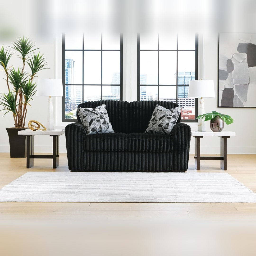 Midnight Madness Onyx jumbo corduroy loveseat with accent pillows, styled in a loft living room with tall black-framed windows