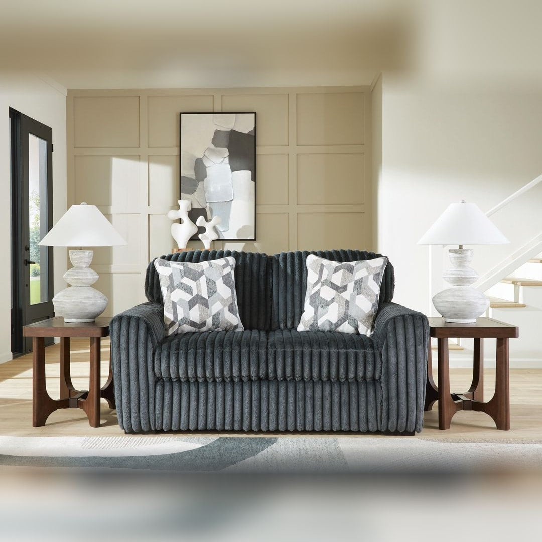 Midnight Madness Gunmetal jumbo corduroy loveseat with accent pillows, styled in a paneled living room between dark wood side tables