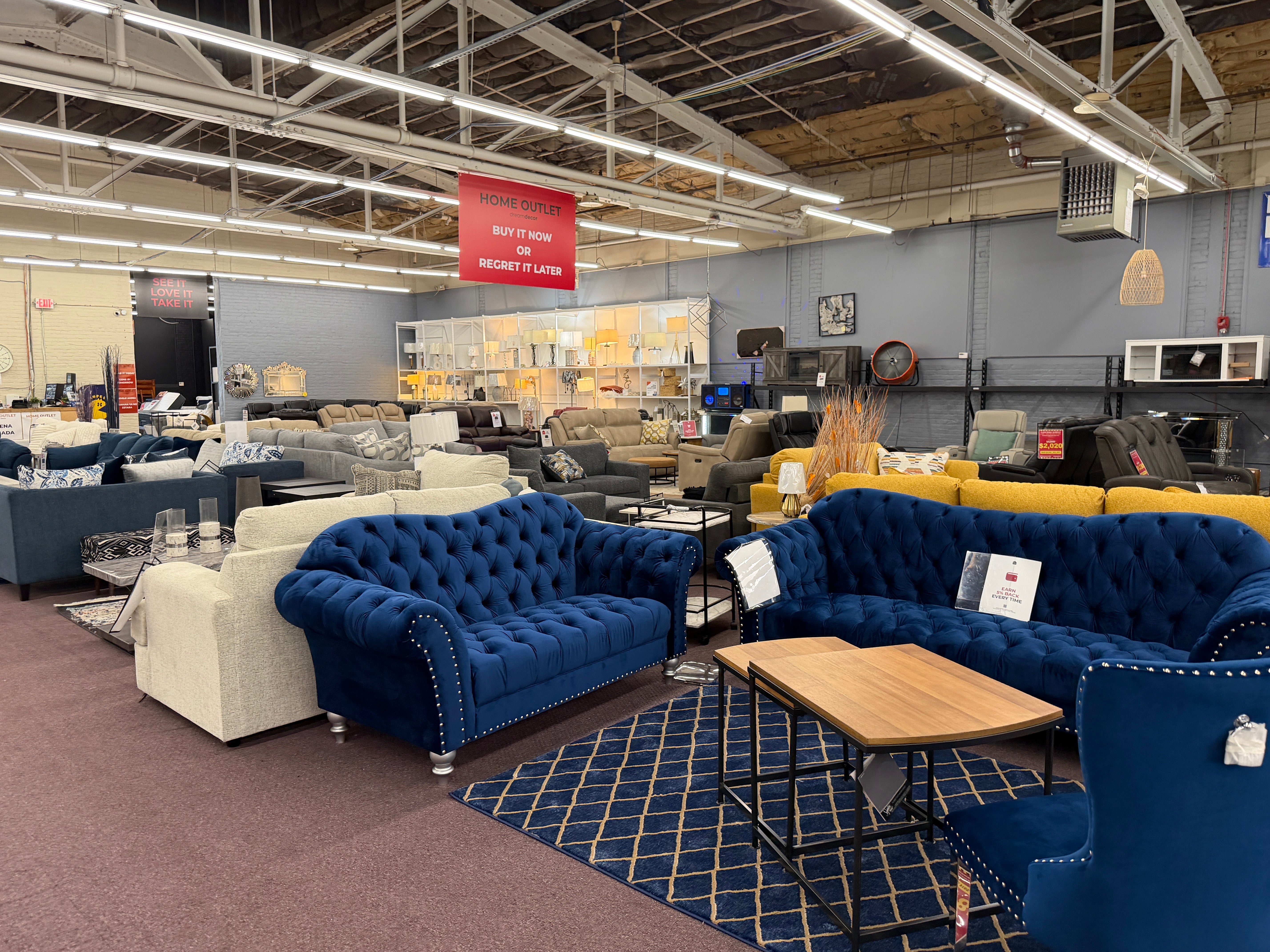 Sofas, sectionals and lamps on the Outlet sales floor under a Buy it now or regret it later sign