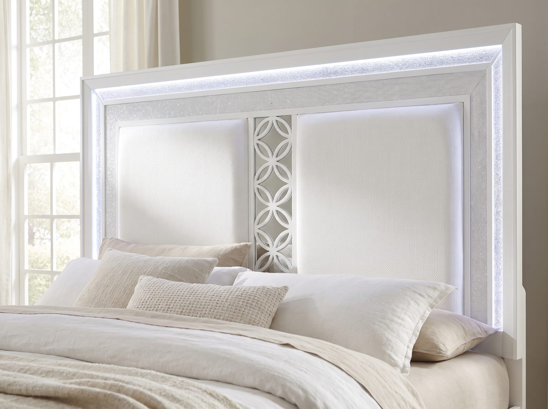 Close detail of the Abigale headboard in crisp white - quilted white upholstered panels, mirrored circular-lattice center inset, and the lit LED crystal-inlay trim running around the frame